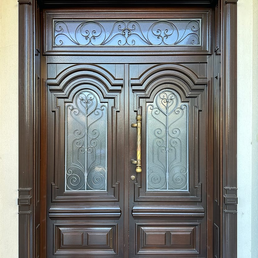 Ușă dublă de intrare, cu panouri profilate, supralumină și feronerie decorativă.