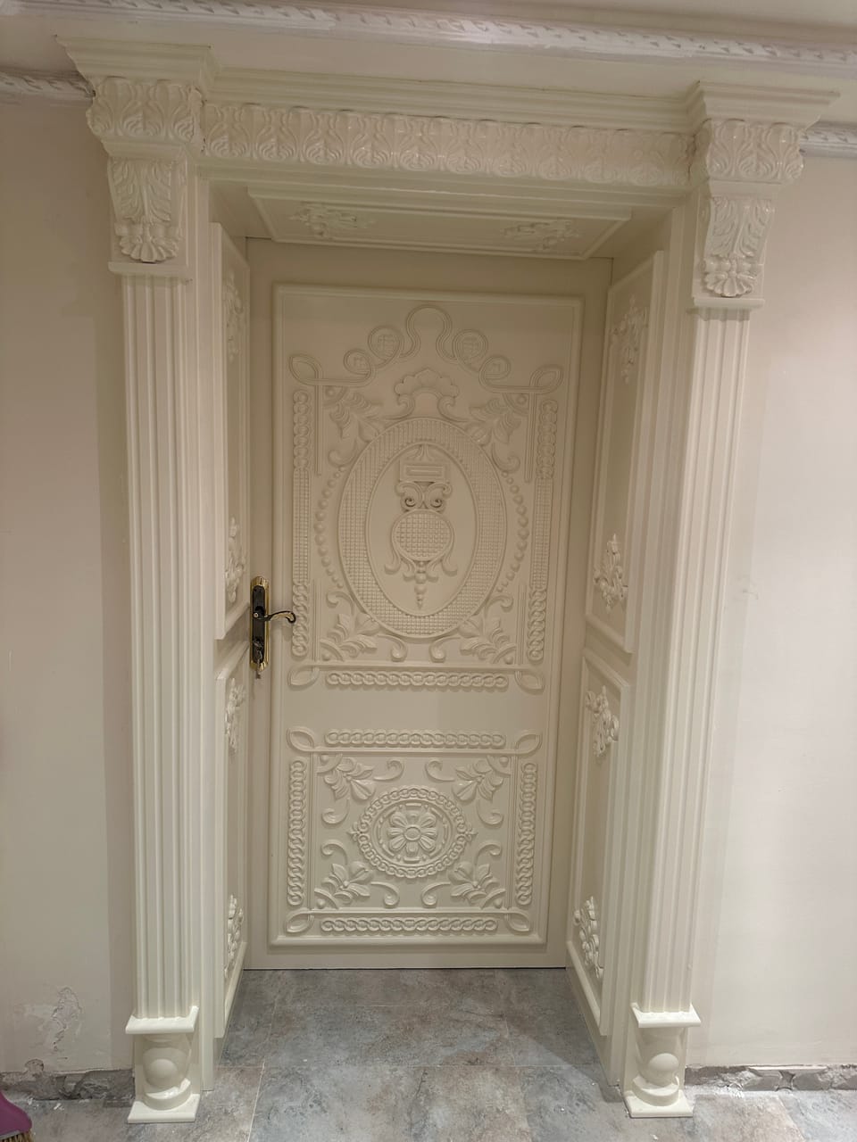 Ușă albă cu panouri cu ornamente în relief, încadrată de pilaștri canelați și o cornișă decorată.