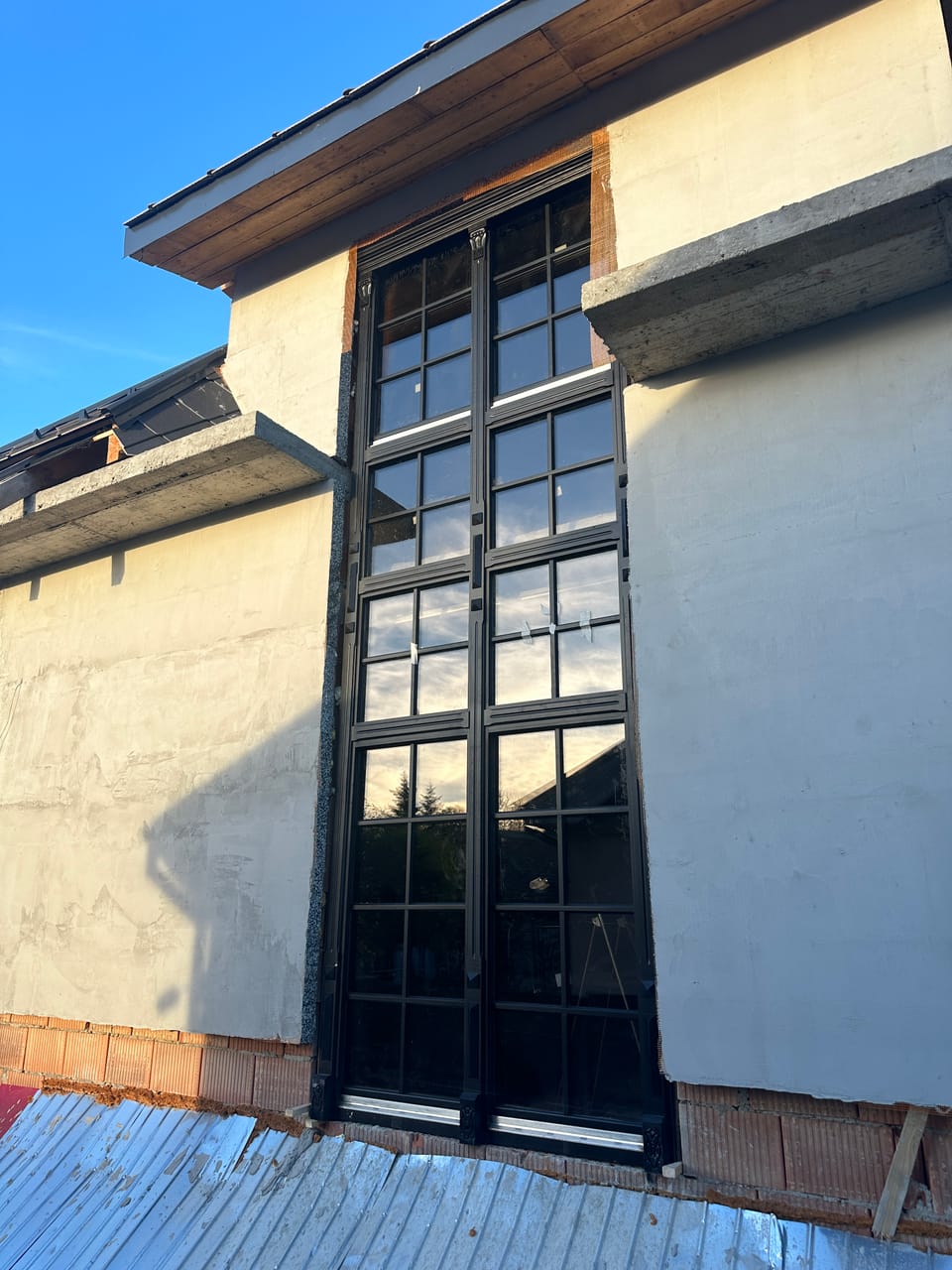 Fereastră înaltă închisă la culoare, cu multe geamuri împărțite de baghete, pe o fațadă.
