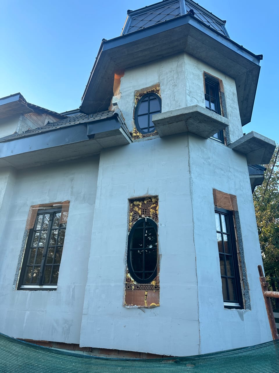 Ferestre închise la culoare cu baghete, inclusiv două ferestre ovale, pe fațada unui turn cu acoperiș în pantă.