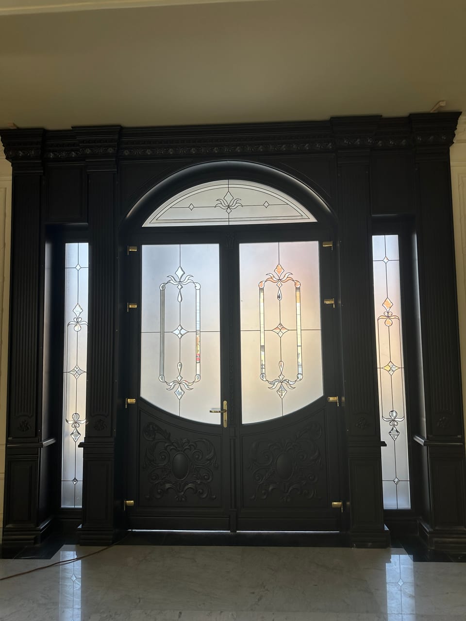 Intrare cu ușă dublă închisă la culoare, supralumină arcuită, geamuri decorative, lumini laterale și coloane.