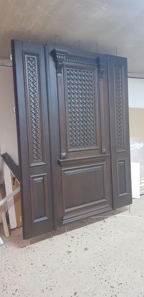 Ușă maro închis cu panou central cu model împletit și două panouri laterale, sprijinită în atelier.