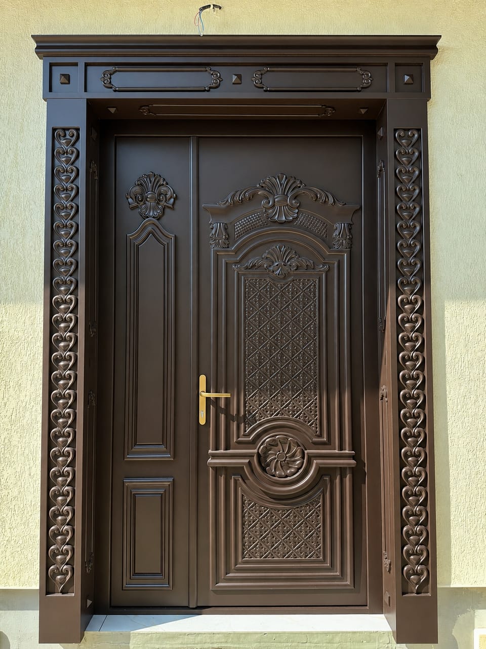 Ușă dublă maro închis cu panouri profilate, ornamente în relief, mâner auriu și ancadrament cu motiv de inimi.